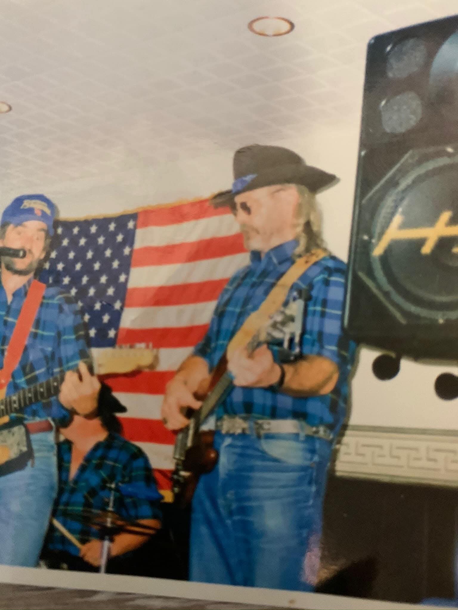 Two country musicians playing guitars beside a stage speaker